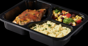 Three-compartment black plastic food tray with a meal of mixed vegetables, rice, and a protein, meat serving.