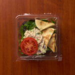 1 Compartment Plastic Cold Tray containing Tuna Salad, a Tomato slice & Pita pieces with film lid top