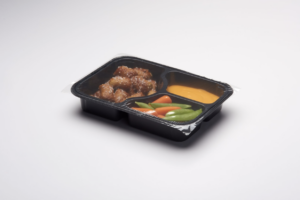 Student meal of pretzel bites, nacho cheese sauce, and mixed vegetables in a three-compartment black plastic tray.