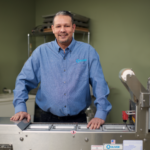 Service Team member Angel, standing in front of an Oliver Heat Sealing machine